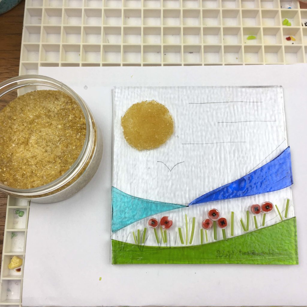 Placing the fine amber frit in place on top of the glastac glue to represent the sun.